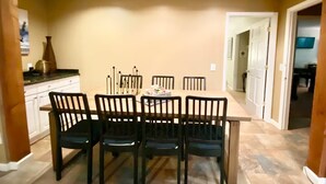 Un comedor con una mesa de madera y seis sillas, un florero en la encimera, y una puerta que da a otra habitación.