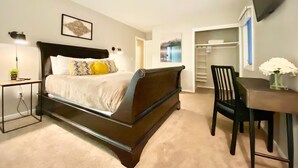 Un dormitorio con cama, mesita de noche, lámpara y una silla. Se observa un armario con estantes y un televisor montado en la pared.