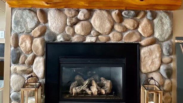 Una chimenea de piedra con repisa de madera, un reloj y dos faroles.