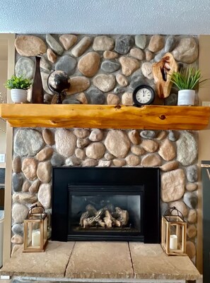 A stone fireplace with a wooden mantel shelf, a clock, and two lanterns. - Perfect location family getaway in Northern MI! (Boyne Falls)