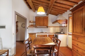 A kitchen with wooden cabinets, a dining table, chairs, and a hanging light fixture. - Tenuta Branca – Torrione Spacious Apartment with Pool in Chianti (San Casciano in Val di Pesa)