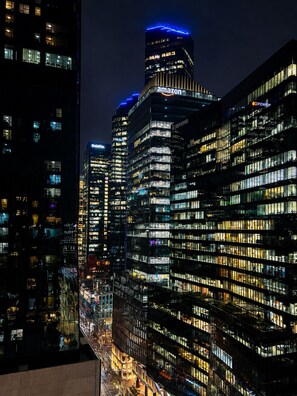 Un paisaje urbano nocturno con edificios altos iluminados, incluyendo nombres corporativos reconocibles.