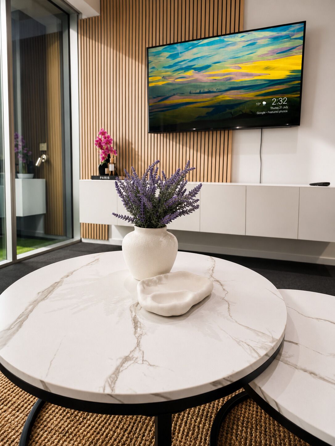 Un intérieur moderne avec une table ronde en marbre, une plante en pot et un téléviseur à écran plat fixé au mur.