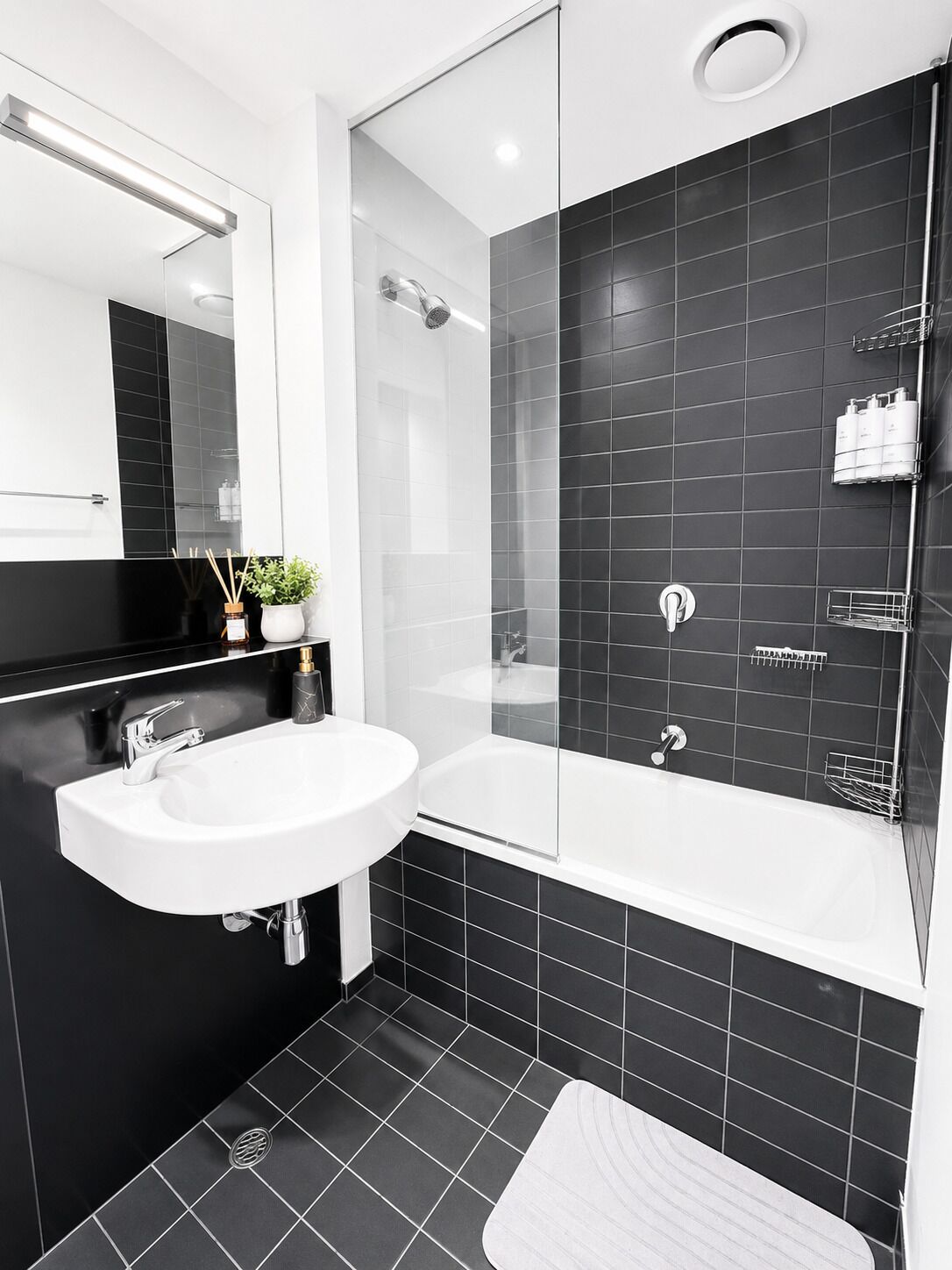 A modern bathroom with a white sink, a glass-enclosed shower, and black tiled walls.