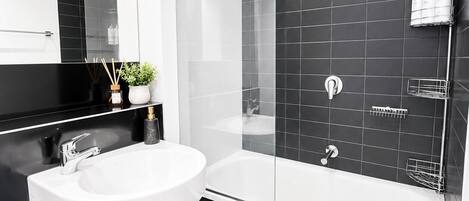 A modern bathroom with a white sink, a glass-enclosed shower, and black tiled walls.