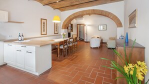 A spacious kitchen with white cabinetry, a wooden island, and a dining area with chairs. - Tenuta Branca – Voltine Apartment: Comfort and Pool in Chianti (San Casciano in Val di Pesa)