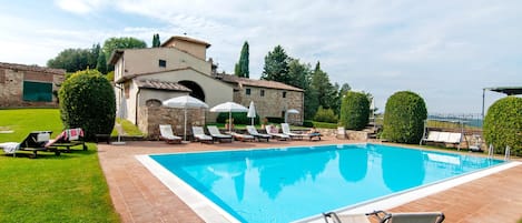 A swimming pool with lounge chairs and a stone building in the background.