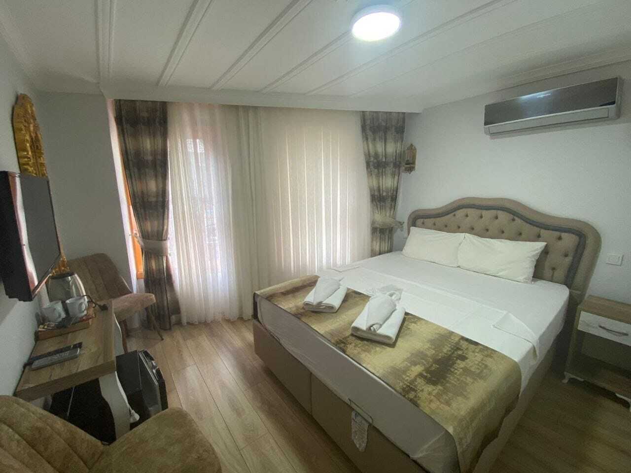 A hotel room with a bed, a desk with a chair, a television, and an air conditioning unit.