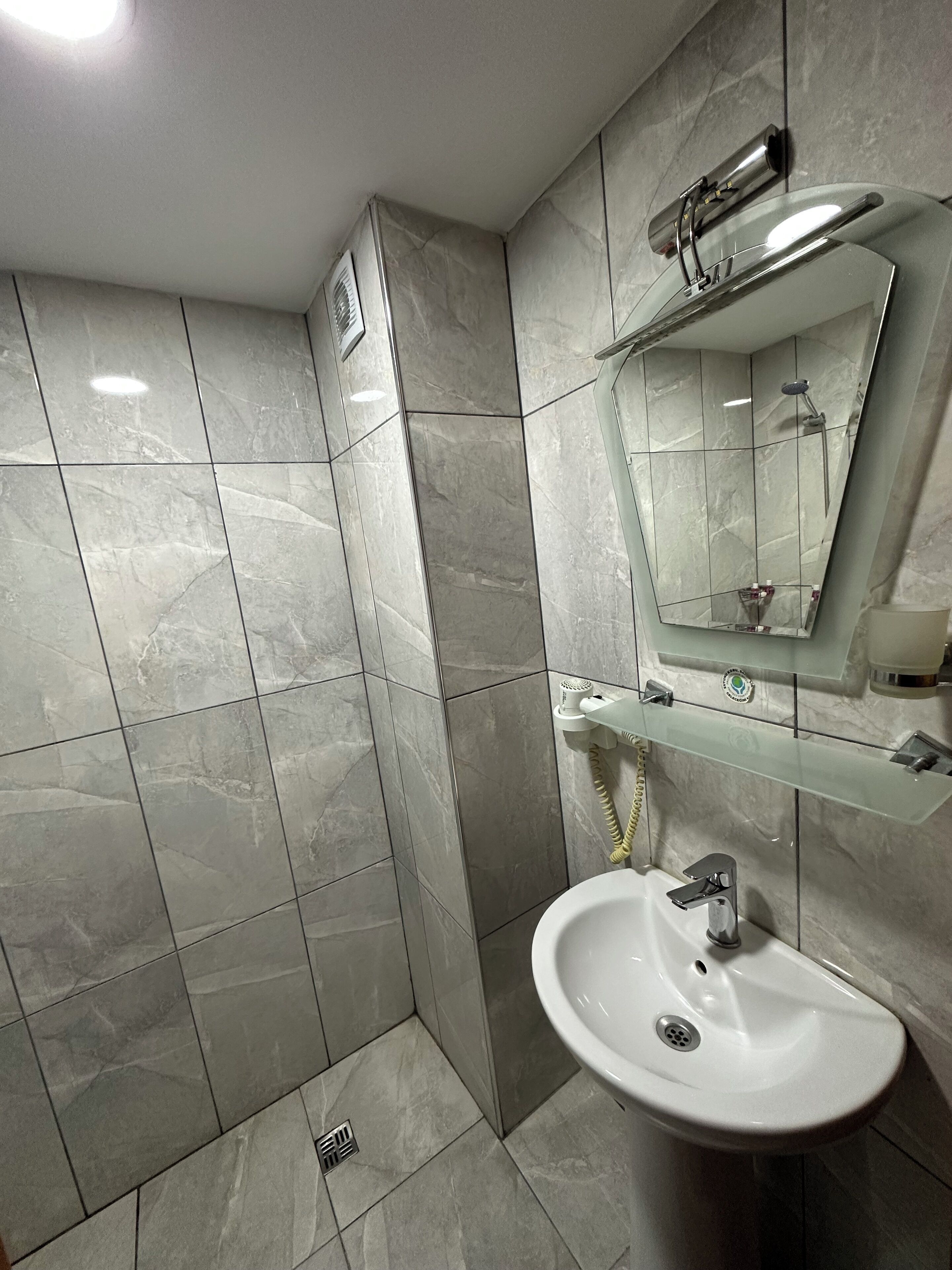 A modern bathroom with a white sink, a glass shelf, a mirror, and a shower.
