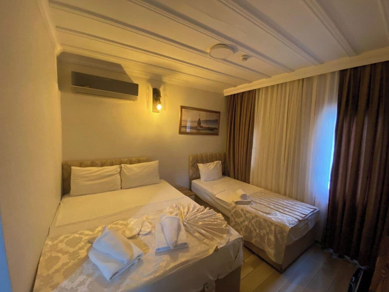 Una habitación de hotel con dos camas, un cuadro en la pared y una ventana con cortinas.