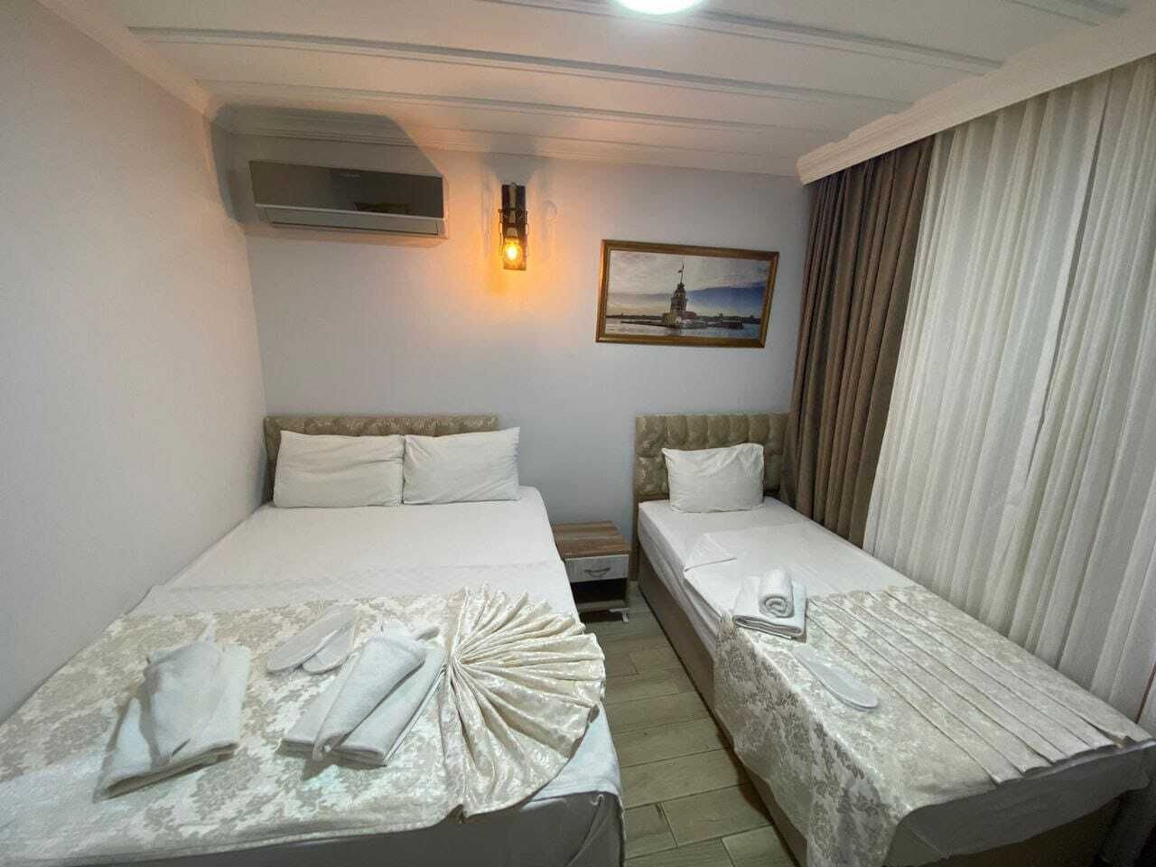 Une chambre d’hôtel avec deux lits simples, une table de chevet, une lampe, un tableau et une fenêtre avec des rideaux.