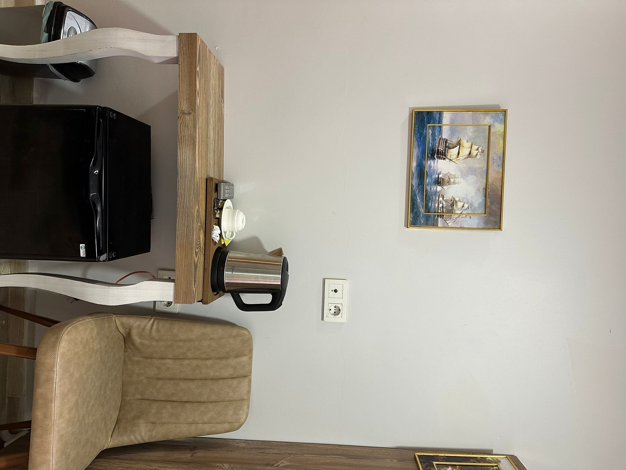 A room with a wooden-framed TV, a coffee machine, a framed painting, and a power outlet.