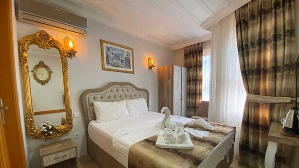 A hotel room with a large bed, a nightstand, a mirror, and a wall-mounted light. - Tree house hotel (Istanbul)