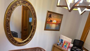 A room with a round wooden table surrounded by wicker chairs with red cushions, a large ornate mirror, a painting of a sunset, and a desk with magazines and a laptop. - Tree house hotel (Istanbul)