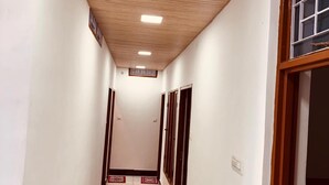 A hallway with white walls, wooden ceiling, and a tiled floor. - Hotel Kashi Ganga (Bhatwari)