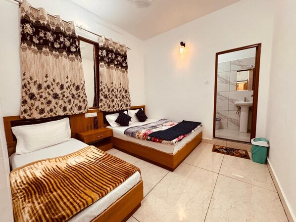 A bedroom with two beds, a nightstand, a mirror, and a bathroom visible through an open door. - Hotel Kashi Ganga (Bhatwari)