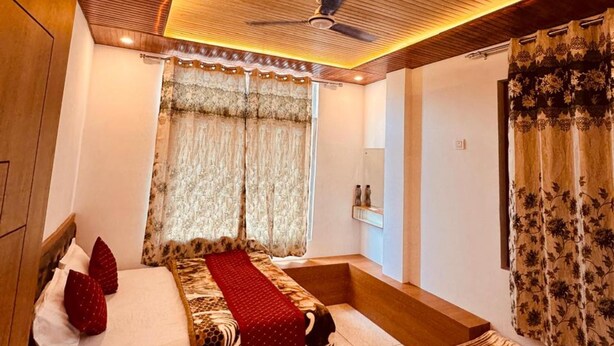 A bedroom with a bed, bedside table, and a ceiling fan. - Hotel Kashi Ganga (Bhatwari)