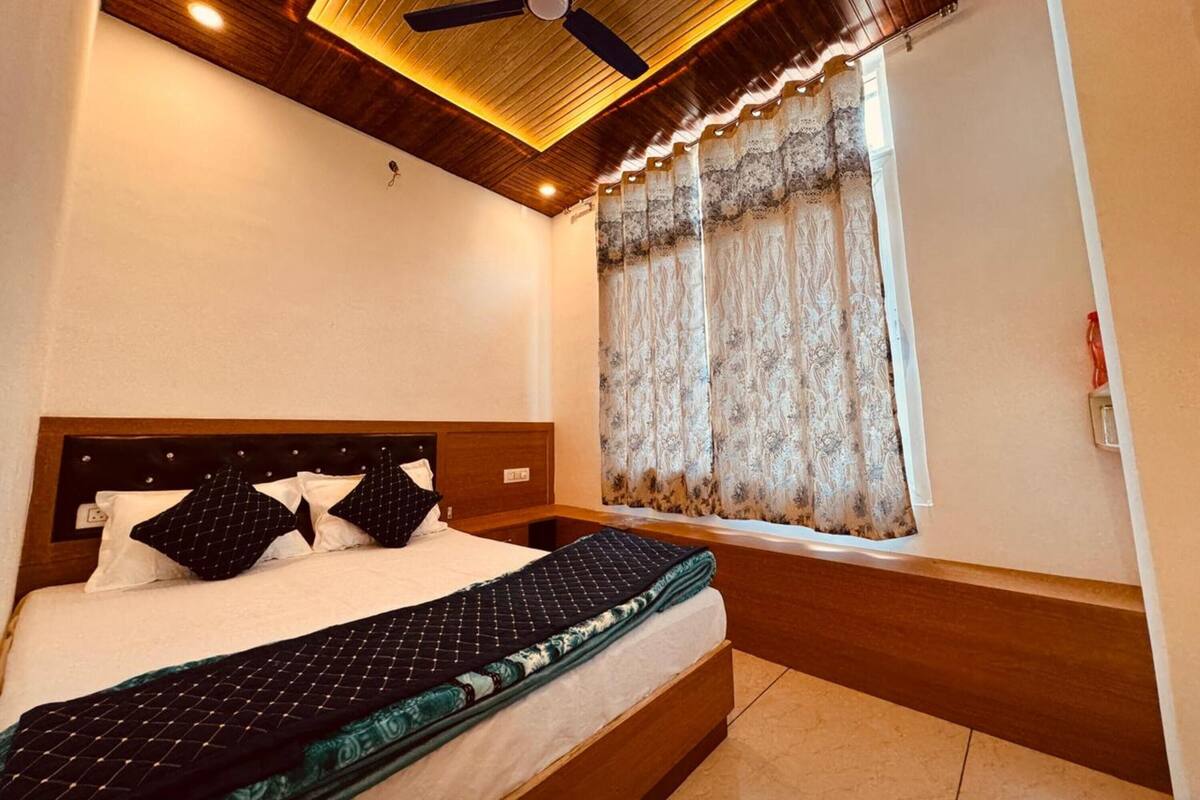 Une chambre à coucher avec une tête de lit en bois, un lit recouvert d’une courtepointe matelassée, un ventilateur de plafond et une fenêtre agrémentée de rideaux à motifs.