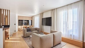 A modern living room with a sofa, a flat-screen TV, and a dining area with a kitchen in the background. - Sublim Penthouse  Trocadero Tour Eiffel (Paris)