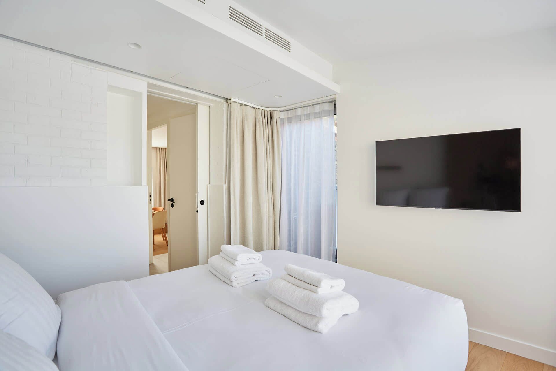 A hotel room with a bed, a TV mounted on the wall, and a door leading to a bathroom.