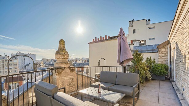 A rooftop terrace with outdoor seating, a decorative column, and a view of the cityscape. - Sublim Penthouse  Trocadero Tour Eiffel (Paris)
