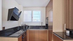 A compact kitchen with a black countertop, wooden cabinets, a window with blinds, and a stainless steel kettle. - Sublim Penthouse  Trocadero Tour Eiffel (Paris)