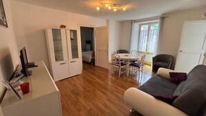 Een woonkamer met een bank, een eettafel met stoelen, een witte garderobe en een televisie.