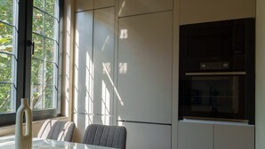 A modern kitchen with built-in appliances, a dining area with a table and chairs, and large windows allowing natural light. - Designer suites on Mashtots avenue (Yerevan)