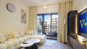 Un soggiorno moderno con un divano componibile, un tavolino rotondo, una televisione a schermo piatto e una grande finestra vista sugli edifici.