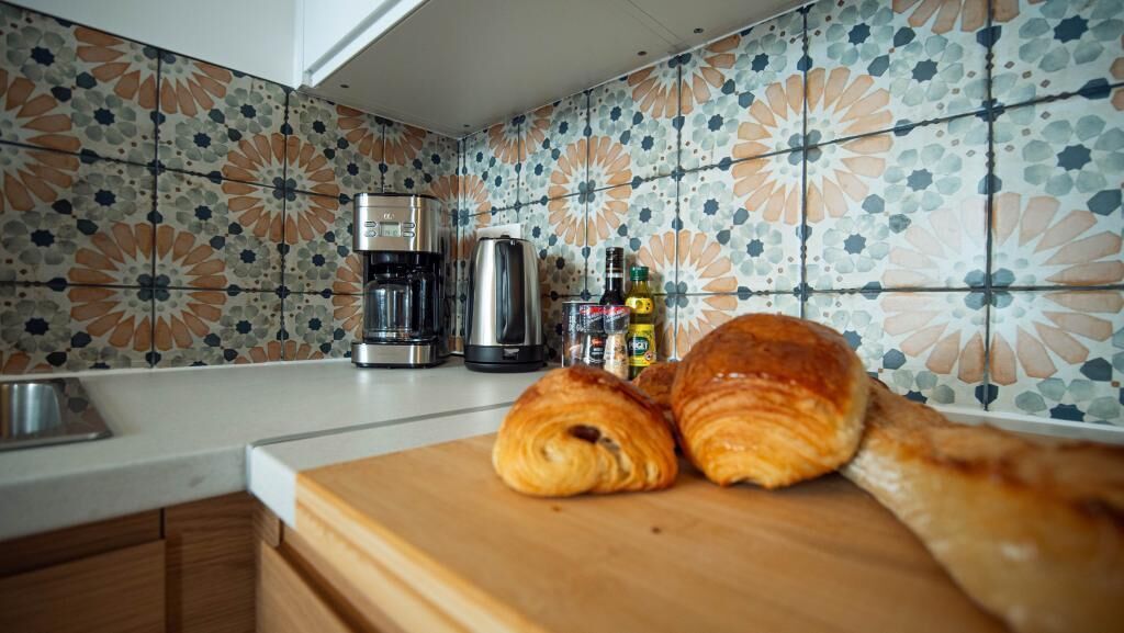 Una cucina con una macchina da caffè, un bollitore e un tagliere con dei cornetti.