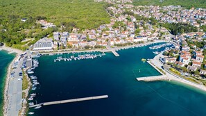Vue aérienne d’une ville côtière avec un port de plaisance, des immeubles résidentiels et une route menant au port.