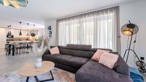 Un salon moderne comprenant un canapé d’angle, une table basse et un coin repas avec des chaises et une table.