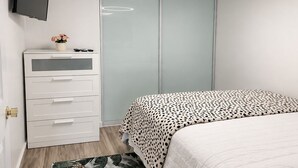 Ein Schlafzimmer mit einem Bett, einem Schminktisch, einem Fernseher, einer Deckenleuchte und einer Klimaanlage.