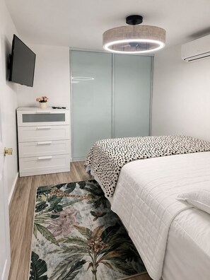 Une chambre à coucher comprenant un lit, une commode, un téléviseur, un luminaire au plafond et un climatiseur.