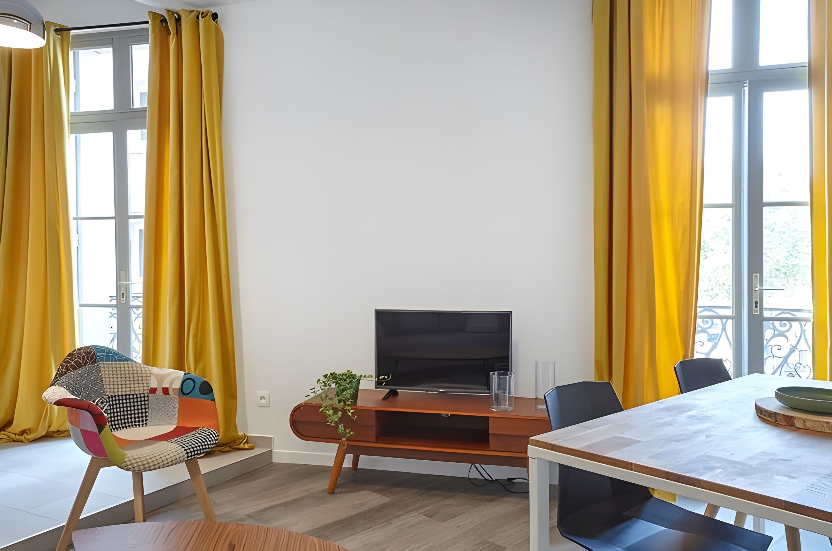 A modern living room with a TV, a dining table, and yellow curtains.