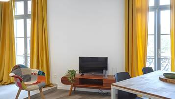 A modern living room with a TV, a dining table, and yellow curtains.