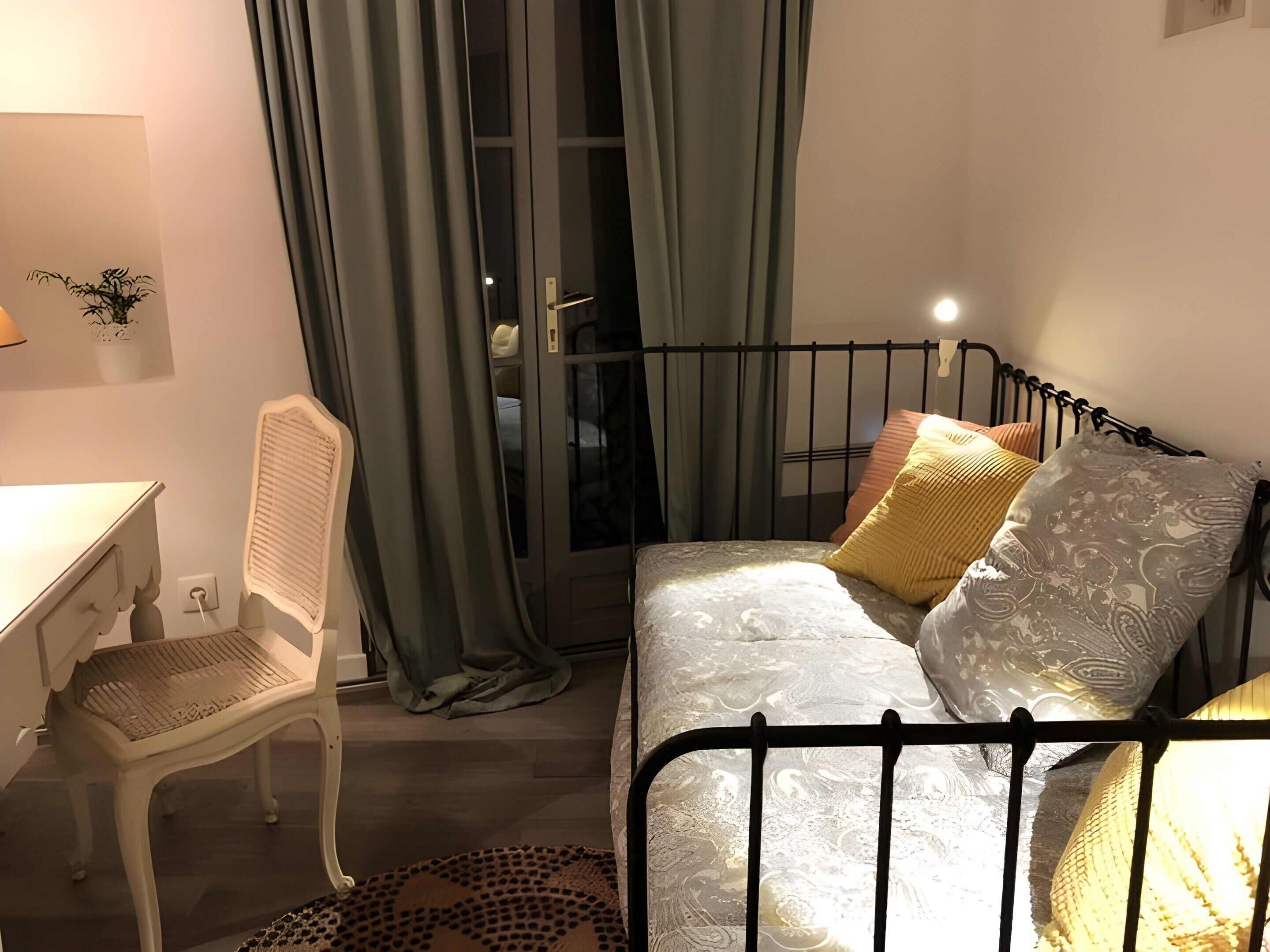 Un dormitorio con cama, escritorio y silla. Se aprecia una ventana con cortinas, una planta en la pared y una lámpara.