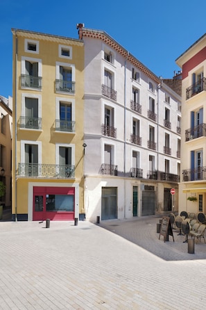 Un edificio de varios pisos con balcones, una puerta roja y un patio empedrado.