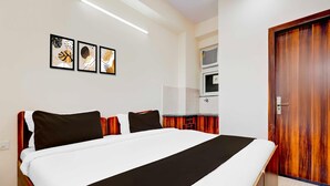 A hotel room with a large bed, a wooden headboard, a flat-screen TV, a microwave, and a wooden door. - Super Hotel O Sadar Bazar Gurgaon (Gurugram)