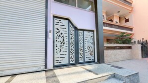 A building with a closed shutter door, a set of steps leading to a gated entrance, and a balcony with plants. - Super Hotel O Sadar Bazar Gurgaon (Gurugram)