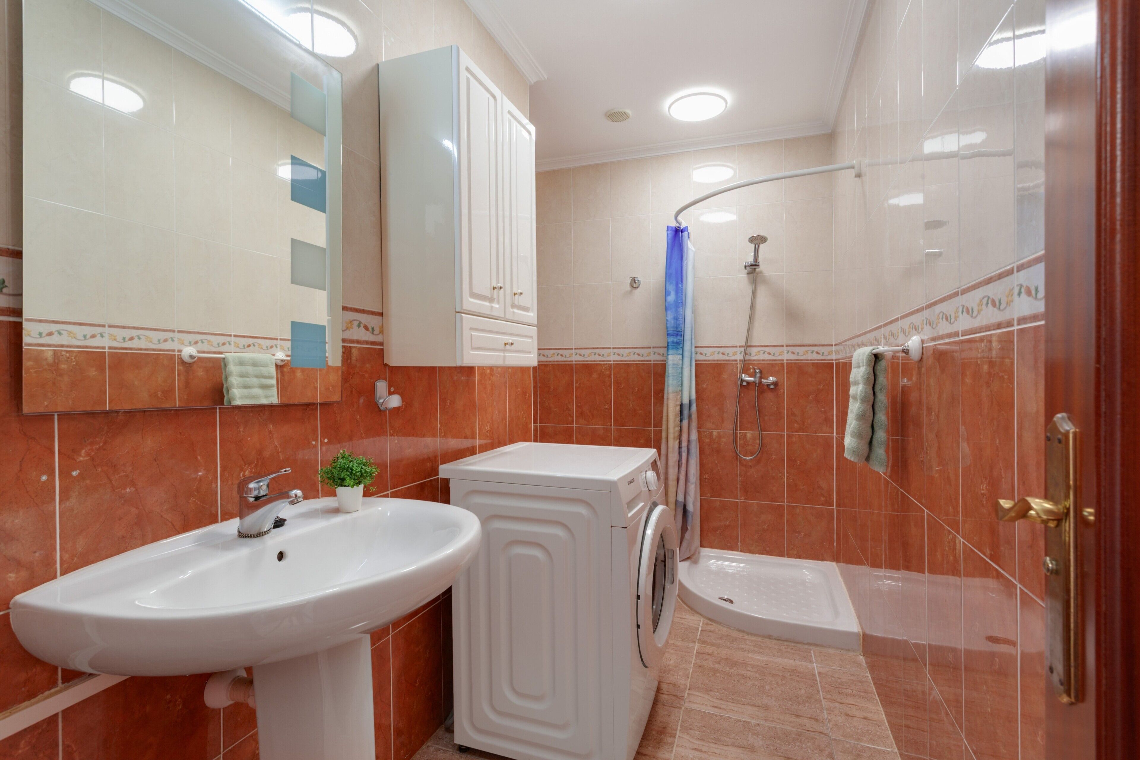 Un baño con lavamanos, lavadora, ducha y espejo.