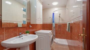 Un baño con lavamanos, lavadora, ducha y espejo.