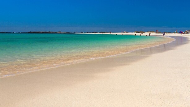 Ein Strand mit klarem türkisblauem Wasser, sandigem Ufer und weiter Ferne.