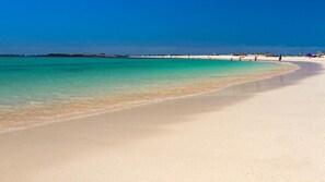 Une plage à l’eau turquoise et limpide, avec un rivage sablonneux et un horizon lointain.