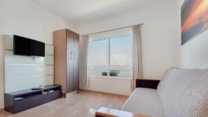 Ein modernes Wohnzimmer mit Flachbildfernseher, einer Couch, einem Schrank und einem großen Fenster mit Vorhängen.
