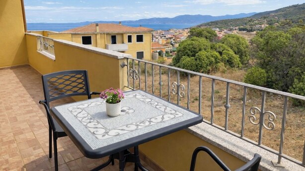 A balcony with a table and chairs, a potted plant, and a view of a town and mountains. - Sea View Apartment with Terrace - Castelsardo | Montemarina (Castelsardo)