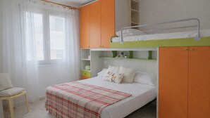 A bedroom with a bunk bed, a chair, a bedside table, and a window with sheer curtains. - Sea View Apartment with Terrace - Castelsardo | Montemarina (Castelsardo)