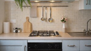 A kitchen with a gas stove, a hanging plant, a wooden cutting board, and a vase with flowers. - Sea View Apartment with Terrace - Castelsardo | Montemarina (Castelsardo)