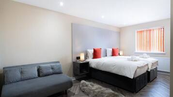 Une chambre à coucher moderne avec un canapé gris, un grand lit avec des oreillers blancs et rouges, une table de chevet avec une lampe et un tapis en fourrure sur le sol.