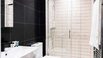 A modern bathroom with a black tiled wall, a white sink, a toilet, and a glass-enclosed shower.